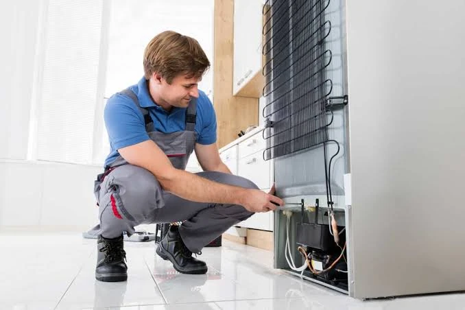 Technician inspecting components behind a refrigerator